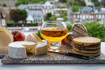 Wall Mural - Cow cheeses of Normandy - camembert, livarot, neufchatel, pont l'eveque and glass of apple cider drink with houses of Etretat village on background, Normandy, France