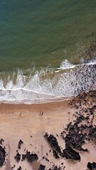 Canvas Print - Aerial view looking down onto views crashing onto a sandy beach. 