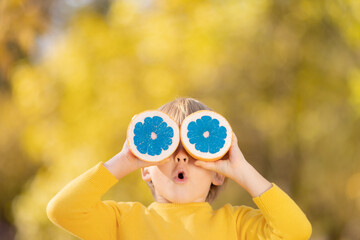 Wall Mural - Surprised child holding slices of orange fruit like sunglasses