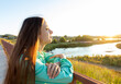 Young girl with loose long hair admiring sunset on river on summer evening in countryside.