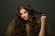 © millaf (Nemchinova) - Brunette beauty. Healthy young woman with long wavy hair touсhing her hair curl on black. Fashion, hair care and beauty concept.