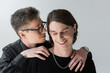 Man in eyeglasses hugging smiling boyfriend with closed eyes isolated on grey.