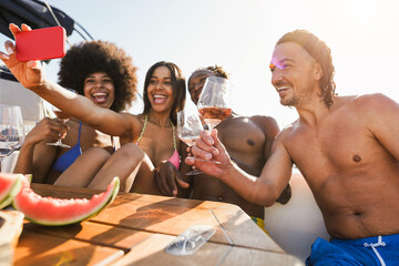 Wall Mural - Happy multiracial friends taking selfie while doing sea tour with sailing boat - Man hand holding glass