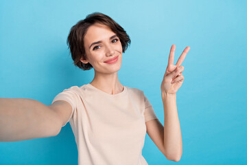 Sticker - Photo of young charming cheery lady take selfie make video for her friends show v sign isolated on blue color background