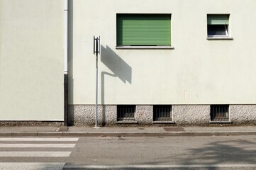 Road sign with shadow on the condominium facade. Paved sidewalk and asphalt street in front. Urban background for copy space