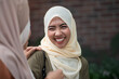 Asian Muslim woman and her friend wear a traditional Muslim hijab outdoors, laughing together