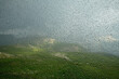 Blick aus einem Fenster das mit Regentropfen bedeckt ist und dahinter eine verregnete Alpenlandschaft 