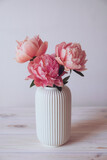 Fototapeta Kwiaty - Beautiful bunch of fresh Coral Charm peonies in full bloom in vase against white background. Minimalist floral still life with blooming flowers.