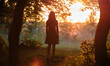 © bilanol - Rear view of young woman in walking alone through dark woods at bright sunset. Nature exploration concept