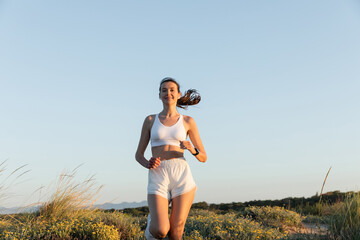 Wall Mural - happy sportswoman in shorts and sports bra listening music and running outside.