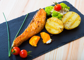 Wall Mural - Fried salmon steak served on slate board with vegetables and egg yolk