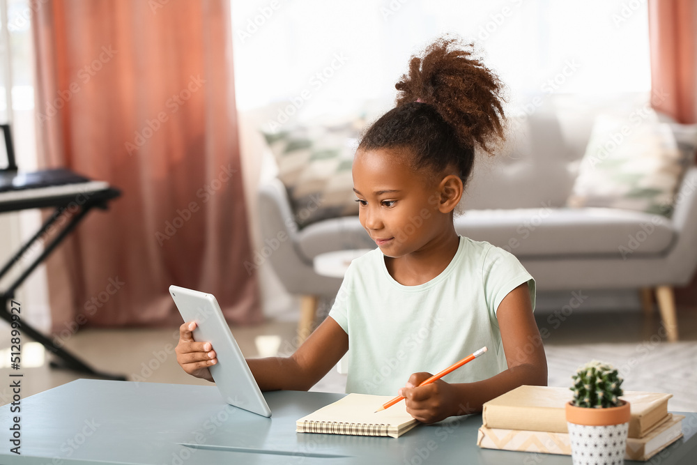 Little African-American girl with tablet computer and notebook at home