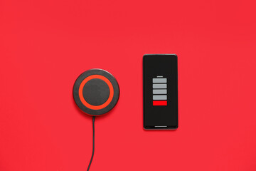 Modern wireless charger pad and uncharged mobile phone on red background