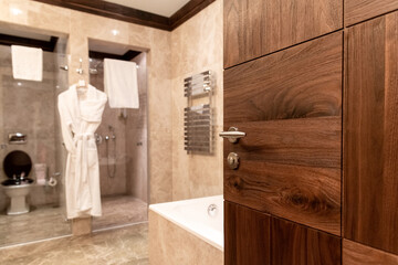 Wall Mural - Wooden door to the bathroom in  hotel or apartament. Open  door to the bathroom, where  white cotton bathrobes hang. Hotel business concept.Out of focus.