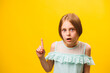 surprised amazed little americana children girl pointing finger up over yellow background.