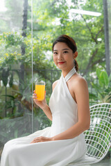 Wall Mural - Portrait of a beautiful woman holding a glass of orange juice looking at you sitting at home