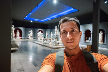 Wall Mural -  Man taking selfie photo in the hall with Greek antique statues of women and goddesses in the interiors of the Archaeological Museum in Antalya