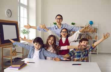 Happy teacher and group of children laughing, shouting hooray and looking at camera. Young woman together with her students having fun excited about start of holiday, summer break or school vacation