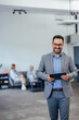 © bnenin - Portrait of a man, standing at the office, smiling for the camera, holding a tablet.