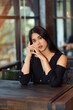 © Other Edge - A woman with long hair, black dress, tanned skin, sits comfortably at a table in the shop