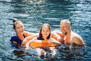 Wall Mural - Happy family having fun on summer vacation. Father, mother and child playing in swimming pool. Active healthy lifestyle concept