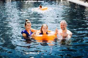 Wall Mural - Happy family having fun on summer vacation. Father, mother and child playing in swimming pool. Active healthy lifestyle concept