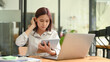 © Prathankarnpap - Focused asian female office worker sitting front of laptop computer and checking information on digital tablet
