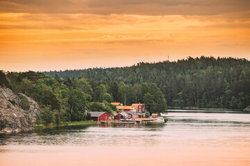 Wall Mural - Sweden. Many Beautiful Red Swedish Wooden Log Cabins Houses On Rocky Island Coast In Summer Evening. Lake Or River Landscape.