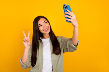 Photo of young pretty cute girl take selfie showing v sign make new post for her blog isolated on yellow color background