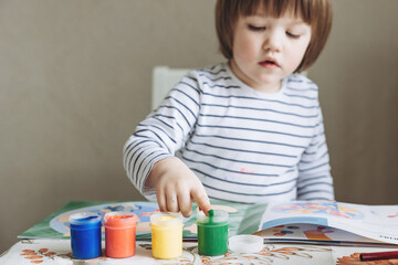 Finger painting. Portrait of cute little boy painting with fingers at home. Close-up of child's hand in colorful paints. Early education concept. Sensory play. Development of fine motor skills.