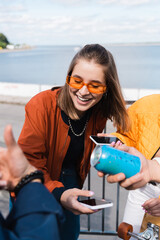 smiling woman in trendy sunglasses holding smartphone with blank screen near friends.