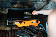 Woman Scrubbing Griddle Plate With Steel Brush Before Cooking A Fish. Cleaning A Greasy Grill.