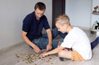 © Julia Jones - A cute boy with a cheerful dad is collecting a puzzle lying on the floor in a room