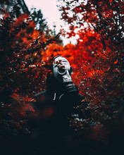 Vertical Closeup Of A Haunting Person Wearing A Gas Mask And A Hoodie In A Red Bush