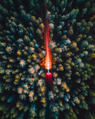 Aerial top view of a car illuminating a highway surrounded by green forest at night