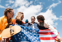 Joyful Multicultural Skaters Holding Usa Flag Under Blue Cloudy Sky.
