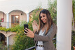 © Hugo - Business girl waving to the camera in a video call on the balcony of a hotel.