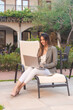 © Hugo - Smiling business girl working with laptop in hotel courtyard - vertical image.