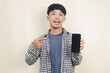 Close-up portrait of happy young Asian male model wearing plaid shirt pointing at phone screen