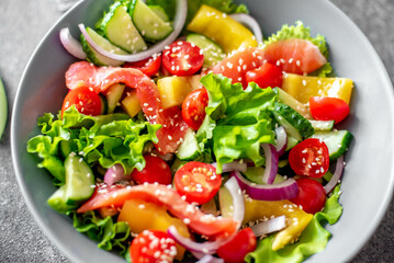 Wall Mural - Salted salmon salad with fresh green lettuce, cucumbers, tomatoes, sweet peppers and red onions on a stone background. Ketogenic, keto or paleo diet lunch bowl.