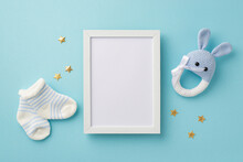 Baby Accessories Concept. Top View Photo Of Photo Frame Tiny Socks Knitted Bunny Rattle Toy And Gold Stars On Isolated Pastel Blue Background With Blank Space