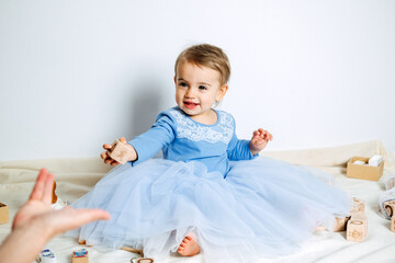 Wall Mural - Cute baby girl in blue princess dress playing toys with mom at home. Kids dresses for birthday holiday.