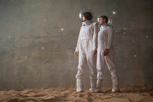 A Man And A Woman In White Futuristic Spacesuits Explore The Planet, Astronauts In An Empty Colony On The Sand, A Holographic Star Map On The Background