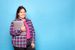 © Lux Images - Young curvy latina woman smiling and holding a laptop, looking at the camera. Indoor studio shot, isolated against a blue background.