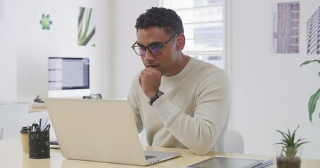 Wall Mural - One focused business man thinking of ideas while working on a laptop in an office. Young designer with glasses browsing the internet for inspiration while planning on a computer in a startup agency