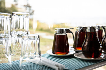 amber maple syrup in glass serving dispensers on saucers next to glassware by a window.