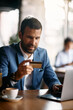 © Drazen - Young businessman using laptop while shopping online with his credit card in cafe.