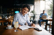© Drazen - Happy businesswoman writing notes while listening music over earphones in cafe.
