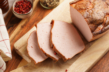 Traditional oven baked bavarian meal leberkäse sliced - meat dish made of corned beef, pork and bacon, finely ground and bakes as a bread loaf, on wooden board on dark wooden table with spices