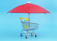 Safety And Protected Shopping Concept. Shopping Cart Under Umbrella On Blue Background.
